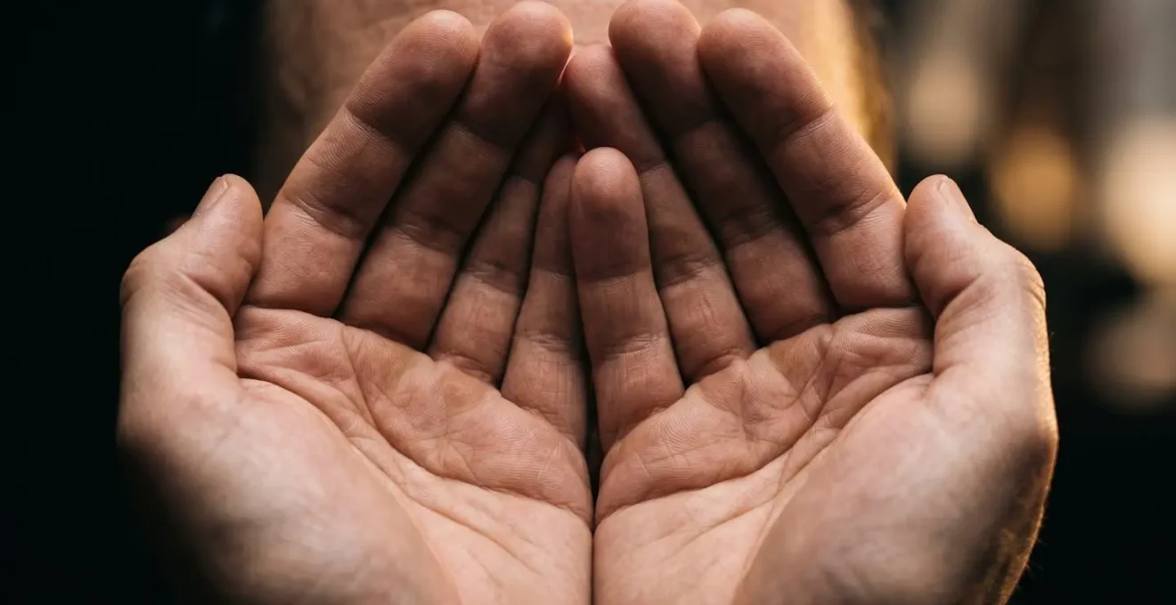 Macro close-up of relaxed hands gently cupped over closed eyes with warm golden light filtering through fingers