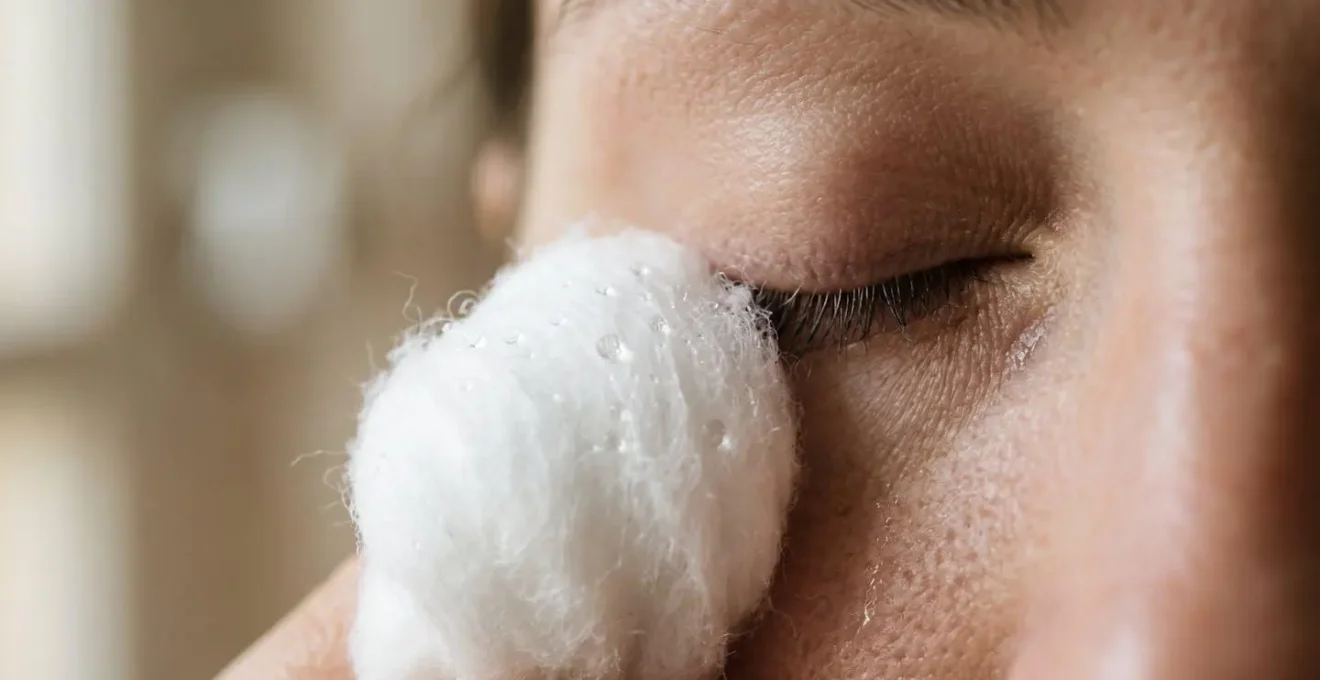 Extreme close-up of clean white cotton ball gently touching eyelid with water droplets visible